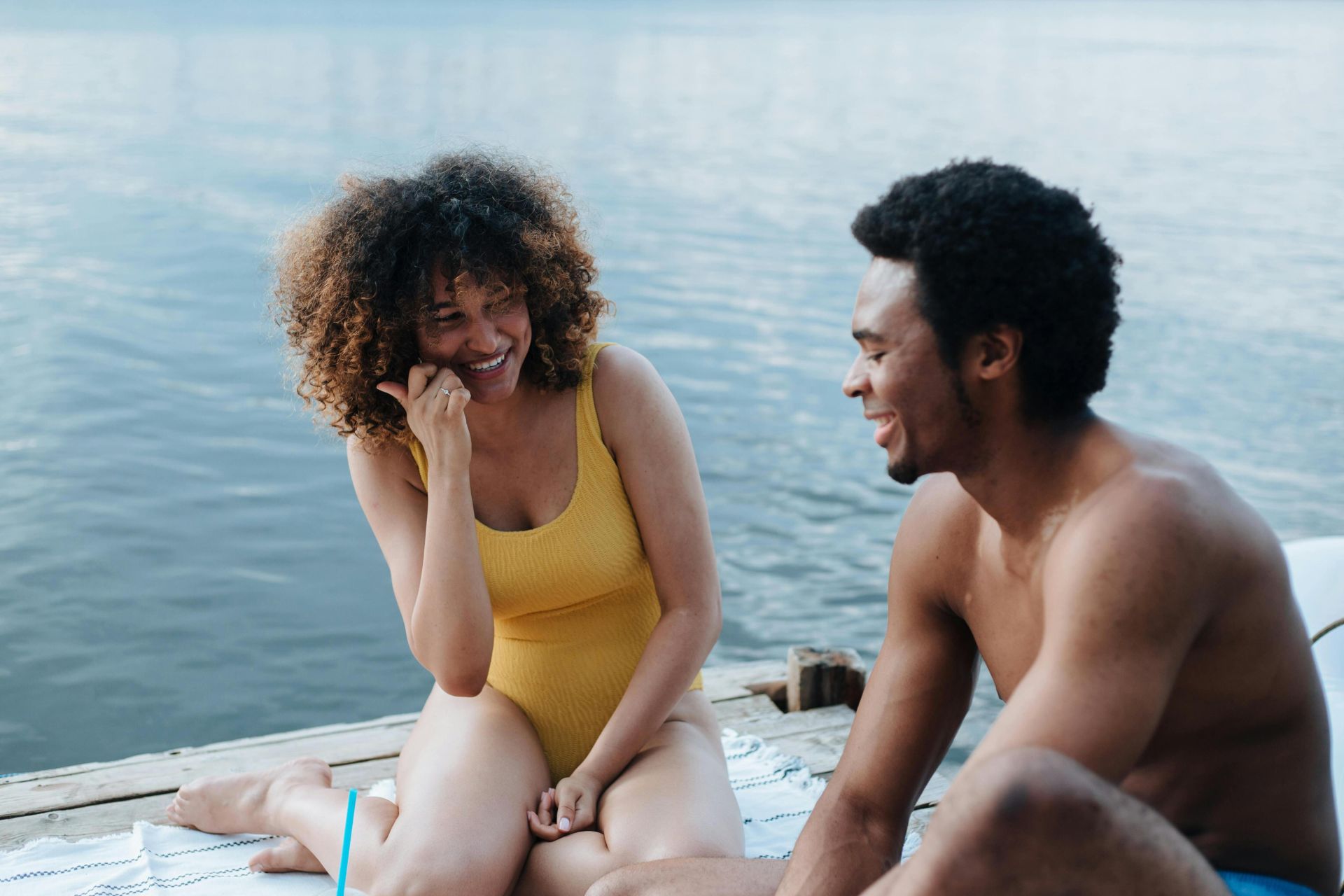 Two friends laughing and enjoying a sunny day sitting on a lakeside dock.